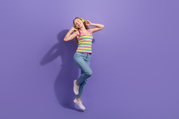 Full size photo of pretty teenager blonde girl headphones dance jump dressed stylish striped outfit isolated on violet color background