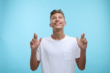 Emotional young man crossing his fingers on light blue background
