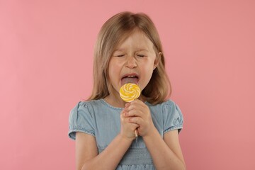 Cute girl licking lollipop on pink background