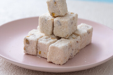 Turkish delights with hazelnuts, pistachios, walnuts, coconut and roses on a pink plate
