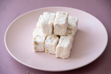 Turkish delights with hazelnuts, pistachios, walnuts, coconut and roses on a pink plate

