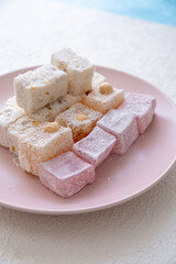 Turkish delights with hazelnuts, pistachios, walnuts, coconut and roses on a pink plate
