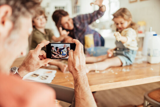 Father capturing a playful moment of the family baking together on his smartphone