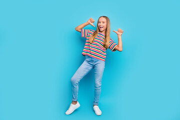 Full size photo of perky optimistic teen girl wear colorful t-shirt denim pants directing at herself isolated on blue color background