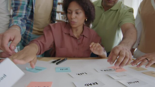 Cropped shot of hands of young diverse university students mixing cards with English verbs while playing educational game for grammar practice in class
