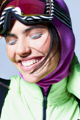 close up of cheerful woman in active wear with balaclava on head smiling on grey background