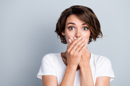 Photo of funky scared woman dressed white t-shirt arms close mouth empty space isolated grey color background