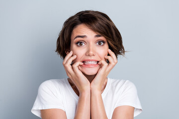 Photo of frightened scared woman dressed white t-shirt biting fingers isolated grey color background
