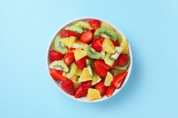 Yummy fruit salad in bowl on light blue background, top view