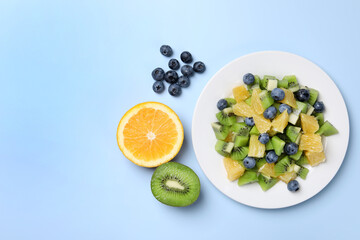 Plate of tasty fruit salad and ingredients on light blue background, flat lay. Space for text