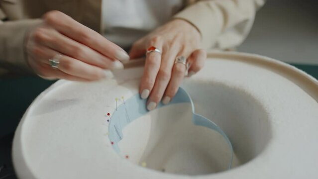 Close-up shot of unrecognizable female hands pinning blue lining into inside of white felt hat