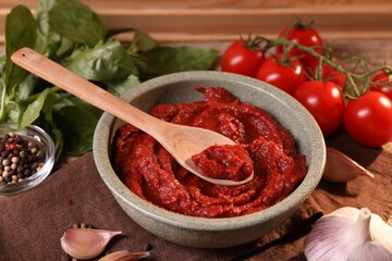 Bowl of tasty tomato paste with spoon and ingredients on table
