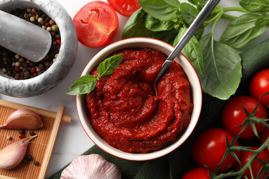 Tasty tomato paste in bowl and ingredients on table, flat lay