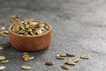 Wooden bowl with peeled pumpkin seeds on grey table. Space for text