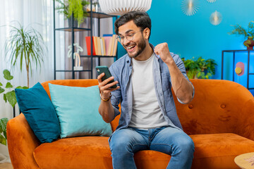 Happy man use mobile smartphone typing browsing say Wow yes, celebrating success victory, winning...