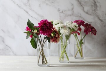 Bouquet of beautiful wild flowers and leaves in vases on white wooden table against marble background
