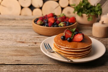 Stack of tasty pancakes with fresh berries and mint on wooden table. Space for text