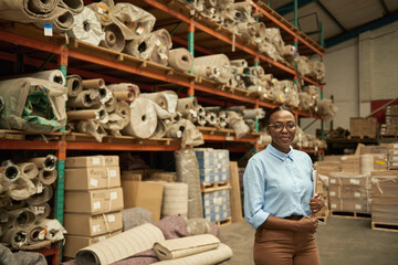 Smiling young African woman standing with a clipboard in a warehouse
