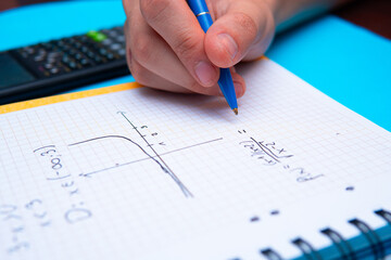 A close-up of a student solving math problems. Notebook with math tasks on a blue background. Solving math problems to practice - obrazy, fototapety, plakaty
