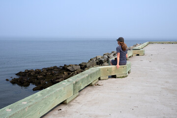 A woman sitting on wharf and looking at the ocean