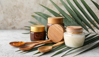 composition with jars of cosmetic products wooden spoons and palm leaf on light background