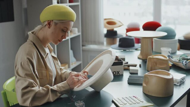 Medium shot of Caucasian young artisan pinning lining inside new hat