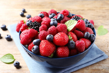 Different fresh ripe berries in bowl on wooden table, closeup