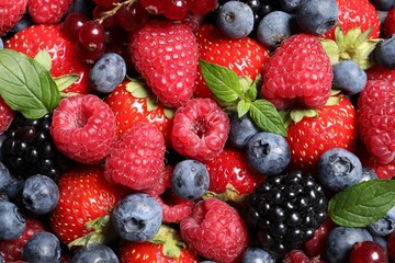 Assortment of fresh ripe berries with green leaves as background, top view
