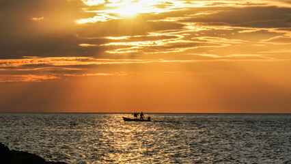 A small fishing boat moored in the middle of the sea during sunset in Thailand.