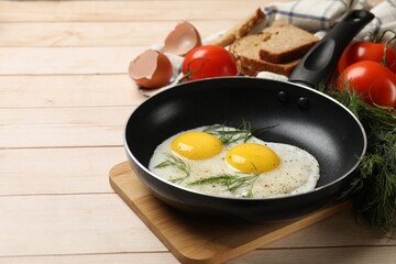 Frying pan with tasty cooked eggs, dill and other products on light wooden table. Space for text