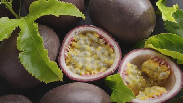 Ripe passion fruits with passion fruit seeds and passionfruit leaves slowly move in the frame on a gray stone table. Nice exotic fruit background for your projects. Macro video shooting.