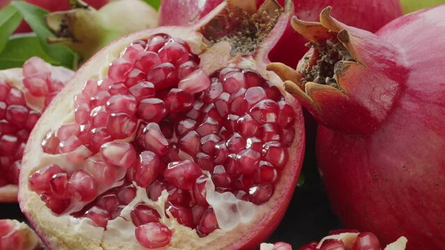 Ripe pomegranate fruits with slices and pomegranate tree leaves slowly move in the frame on a gray stone table. Nice fruit background for your projects. Macro video shooting.