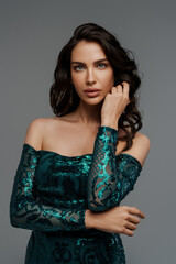 Stunning brunette with a voluminous hairstyle in a graceful green evening gown against a gray backdrop