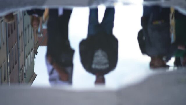 Unrecognizable guy on electric scooter driving through puddle, smearing mirror reflection in water into small waves at city street. Urban autumn life