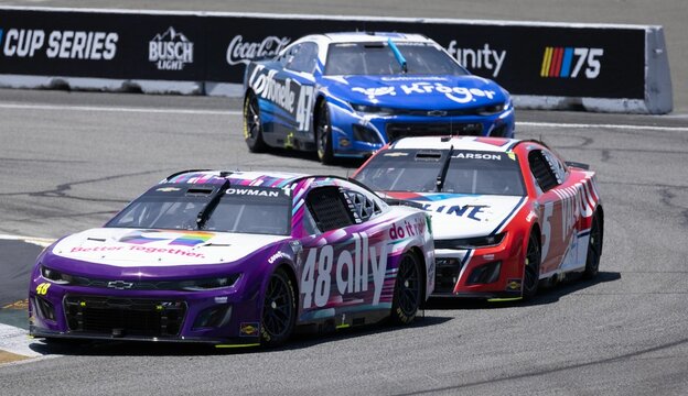 two nascar cars racing down a track next to landowners