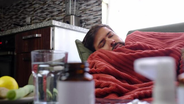 Ginger, lemon, onion and different drugs on table on background sick man. Alternative remedies and traditional pills to treat colds and flu. sick man wrapped in red blanket in background
