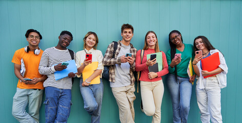 Group of multiethnic young people using mobile phone outdoor. Friends having fun with new trends social media apps. Youth technology addicted. University students isolated in blue background. - obrazy, fototapety, plakaty