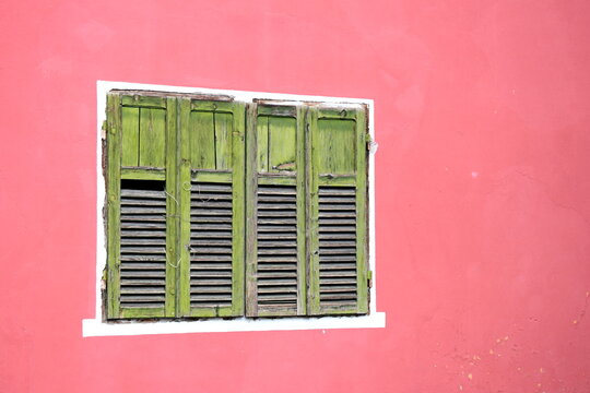 Old red painted house with green closed wooden shutters, dilapidated and ancient