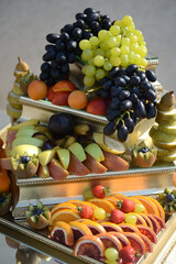 A luxurious fruit buffet with grapes, apples, plums, strawberries, bananas, oranges, and kiwis. A mixture of various sliced fruits. Fruit platter. Table decoration with fruit