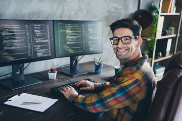 Profile portrait of cheerful guy coding using keyboard create clients support application sit armchair at home office with two monitors