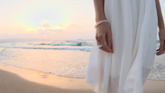 girl in a white dress stands on the beach at sunset. Hands with jewelry close-up.