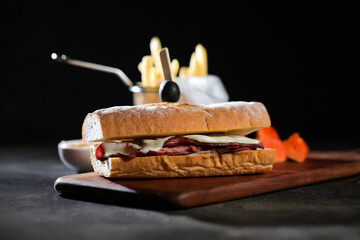 Roasted Beef Sub Sandwich with french fries bucket served on wooden board isolated on dark...