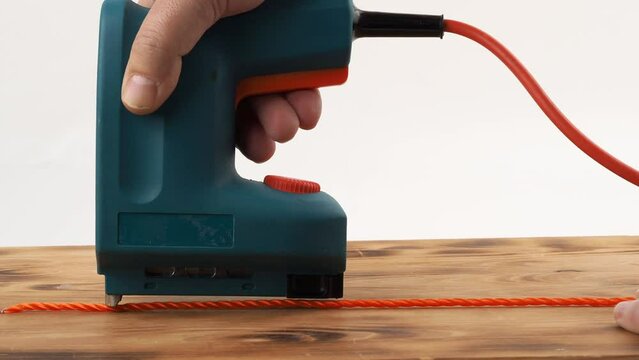Close-up of a man's hand holding an electric stapler and fastening rope to a board. Electric stapler close-up.