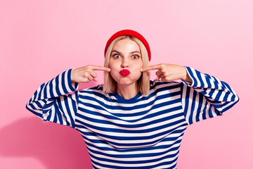 Photo of blonde young girl having fun fooling directing fingers her cheeks playing blow air pouty...