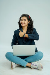 indian girl seated on a white background balances a laptop on her lap
