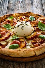 Circle prosciutto burrata pizza with grilled peaches on wooden table
