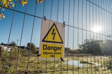 Yellow warning sign displaying danger electric shock risk, affixed to a metal fence, information and safety concept illustration.
