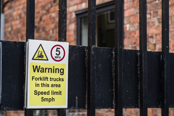 A warning sign attached to a black metal fence indicates the presence of forklift trucks in the area with a speed limit of 5mph.