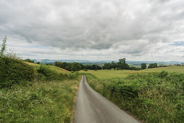 Wide view of Welsh countryside road, with cloudy grey sky. Tourism and travel concept illustration.