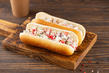 Chopped Italian sandwich in hot dog buns in a wooden board with a paper cup of coffee.